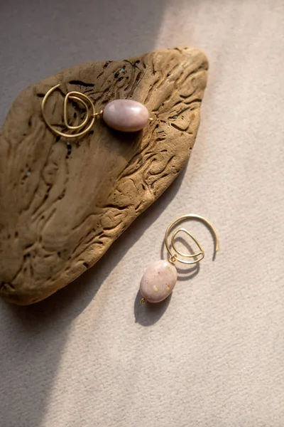 Stylish earrings made natural pink opal stone with Golden brass fittings piece of wood pattern from activity bark beetle. Natural day solar lighting. — Stock Image Stylish Earrings Made Natural Pink Opal Stone Golden Brass Fittings Stock Picture