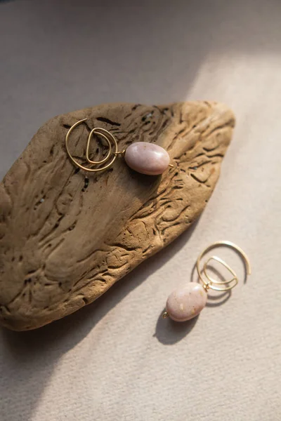 Stylish earrings made natural pink opal stone with Golden brass fittings piece of wood pattern from activity bark beetle. Natural day solar lighting. — Stock Image Stylish Earrings Made Natural Pink Opal Stone Golden Brass Fittings Stock Photo