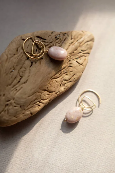 Stylish earrings made natural pink opal stone with Golden brass fittings piece of wood pattern from activity bark beetle. Natural day solar lighting. — Stock Image Stylish Earrings Made Natural Pink Opal Stone Golden Brass Fittings Stock Image