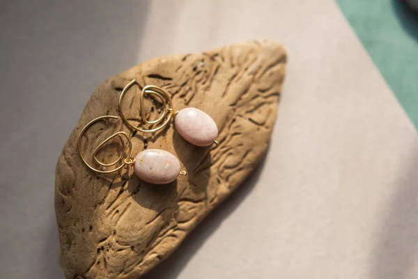 Stylish earrings made natural pink opal stone with Golden brass fittings piece of wood pattern from activity bark beetle. Natural day solar lighting. — Stock Image Stylish Earrings Made Natural Pink Opal Stone Golden Brass Fittings Royalty Free Stock Photos