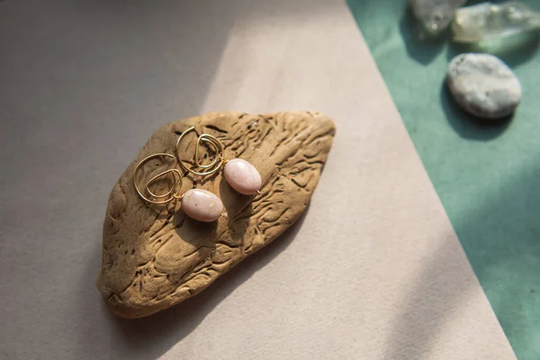 Stylish earrings made natural pink opal stone with Golden brass fittings piece of wood pattern from activity bark beetle. Natural day solar lighting. — Stock Image Stylish Earrings Made Natural Pink Opal Stone Golden Brass Fittings Stock Photo