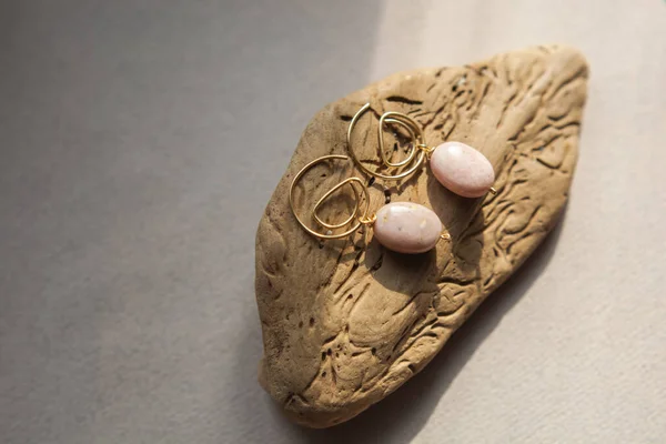 Stylish earrings made natural pink opal stone with Golden brass fittings piece of wood pattern from activity bark beetle. Natural day solar lighting. — Stock Image Stylish Earrings Made Natural Pink Opal Stone Golden Brass Fittings Royalty Free Stock Images