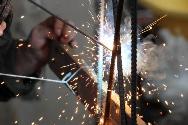 Bir insan koruyucu ekipman olmadan kaynak yaparak çalışır. Eldiven ve maske. Kaynak, metal elementleri tamir ve üretim sırasında güvenilir bir şekilde bağlayabilmenizi sağlar..