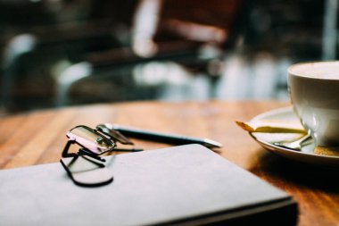 Bir bardak aromatik kahve, telefon ve defter ile bir masada oturan bir adamın eli. İş yemeği