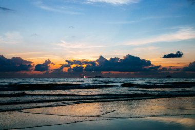 Tatile deniz tarafından güzel gündoğumu. Güneşin ışınları bulutların içinden geçiyor. Haddeleme dalgaları
