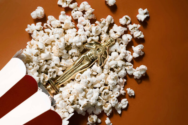 Souvenir golden statuette lies in popcorn on a red background. Film premiere. Rating of the best films. Watch movies. The atmosphere of the cinema.