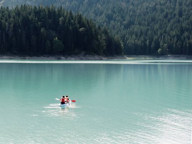 İnsanlar gölü kanoyla geçiyorlar. Güzel doğa. Koyu yeşil köknar, güneş tarafından aydınlatılır..