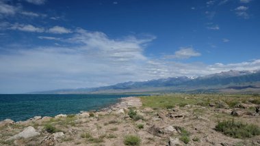 Kayalar ve mavi su ön planda, göl Issyk Kul güney kıyısında doğal Kırgızistan dağ manzarası.