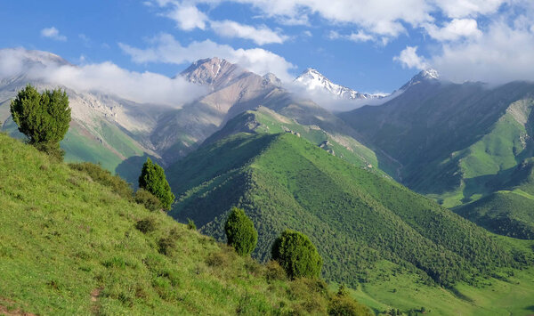 Beautiful mountain landscape with green valleys, glacier peaks, blue sky, and clouds. Bishkek, Kyrgyzstan.