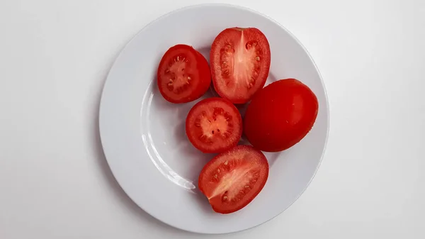 Tomates de corte vermelho encontram-se em uma placa de porcelana branca vista superior — Fotografia de Stock