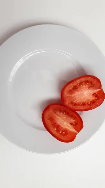무늬없는 흰 접시 위에 붉은 토마토 두 개 반을 올려 놓는다 — 스톡 사진