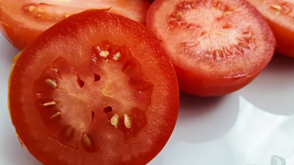 Rote geschnittene Tomaten liegen auf einem weißen Porzellanteller — Stockfoto