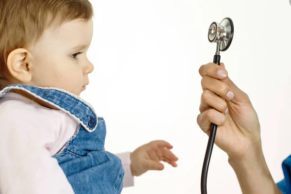 A small child looks at the stethoscope and pulls his hand to it — Stock Photo, Image