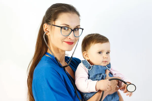 Bir genç kadın doktor onun kollarında, o gülümsüyor, bir bebek tutan ve bir çocuk bir stetoskop ile çalış.