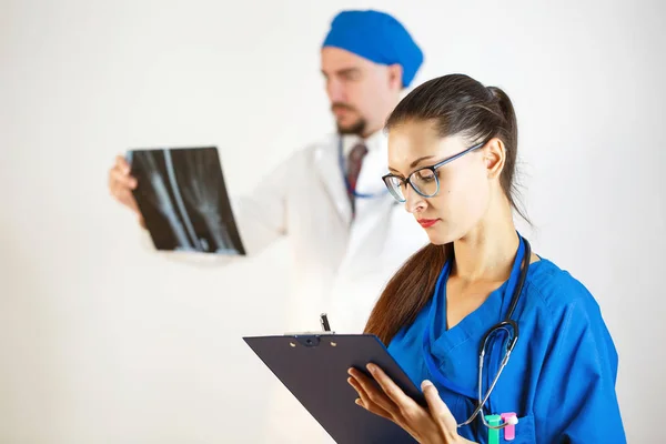 Diagnósticos con la ayuda de rayos X, dos médicos miran los resultados, el médico toma notas a la tarjeta. Fondo blanco — Foto de Stock