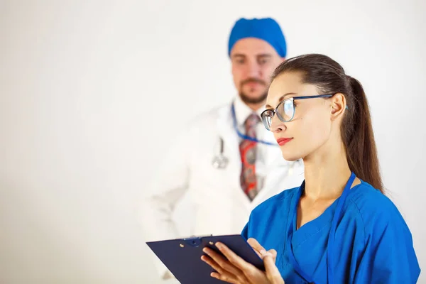 Una doctora con gafas sostiene un diario en sus manos, en el fondo es un doctor masculino. Fondo blanco — Foto de Stock