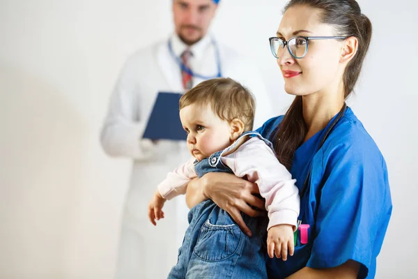Genç hemşire küçük bir çocuk onun kollarında tutar, arka planda bir doktordur