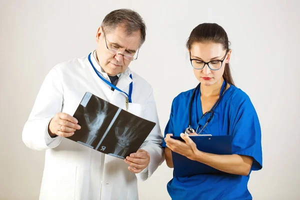 Dos doctores en la clínica, uno está mirando una radiografía, el otro está escribiendo a un diario — Foto de Stock