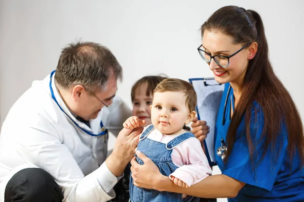 Orvosok megvizsgálják a gyerekek, egy kis gyerek nézi a kamerát, egy fiatal nő orvos mosolyog — Stock Fotó