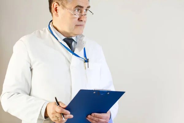 Lékař v bílém plášti vypadá do dálky a obsahuje složky a pero — Stock fotografie