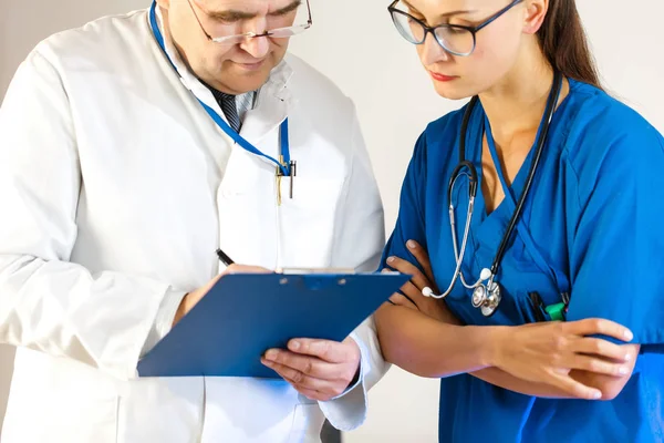 Vedoucí lékař zapisuje data do karty pacienta, další doktor vypadá — Stock fotografie