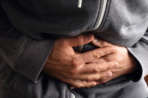 Hombre en ropa gris con dolor de estómago y las manos sobre el vientre — Foto de Stock
