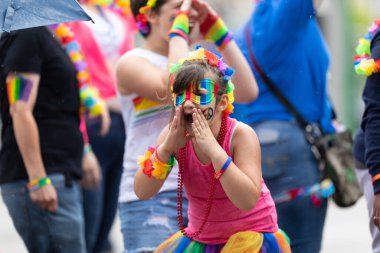 Cincinnati, Ohio, ABD - 22 Haziran 2019: The Cincinnati Pride Parade, gökkuşağı maskeli kız, tören sırasında seyircilere bağırıyor.
