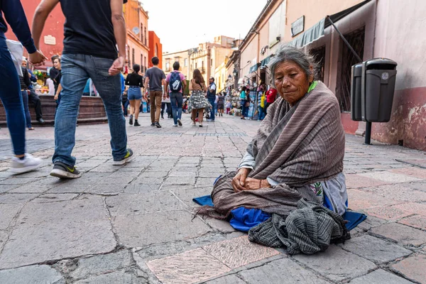 Santiago de Queretaro, Queretaro, Meksika - 24 Kasım 2019: Yaşlı Begar, geleneksel Meksika kıyafetleri giymiş kamera için gülümsüyor ve insanlar andador 5 de Mayo 'nun yanından geçiyor
