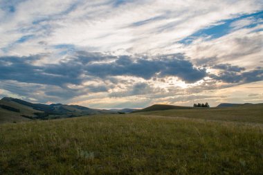 Alacakaranlık gökyüzünün pitoresk bir manzarası ve batan güneşin ışınları altında parlak bulutlar. Arka planda ormanla kaplı dağlar. Sibirya.