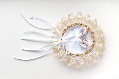 Altın alyanslar kuğularla süslenmiş dantel bir düğün yastığında. Beyaz arkaplanda yakın plan