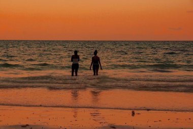 Genç kadınlar kumsalda altın bir günbatımına karşı eğleniyorlar, Zanzibar.