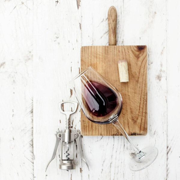 glass of red wine with corkscrew and wine cork on rustic board over white wooden table, Food concept