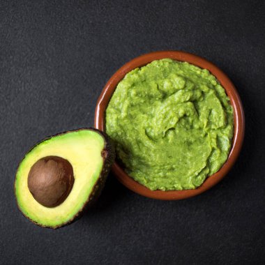 Geleneksel Meksika Dip sos Guacamole ile bir kasede Yarım avokado siyah arka plan üzerine düzenlenen. Üstten görünüm
