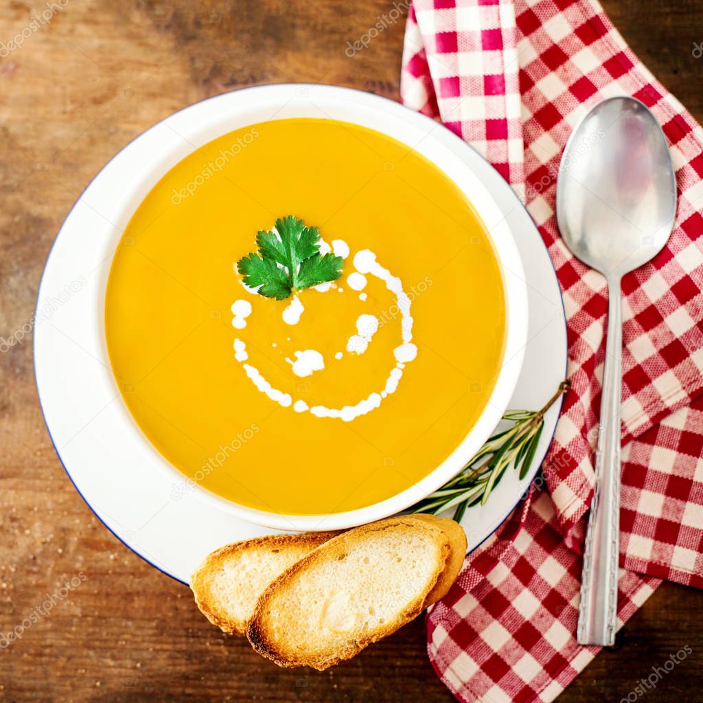 Bowl of vegetable yellow soup with parsley and croutons over wooden background.  Autumn Pumpkin and carrot soup with cream. Copy spac