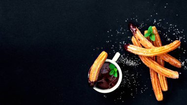 Siyah bir arka plan üzerinde şeker ve çikolata soslu churros. Caner
