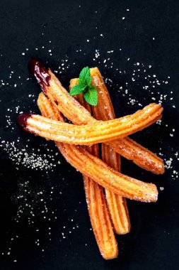 Siyah bir arka plan üzerinde şeker ve çikolata soslu churros. Caner