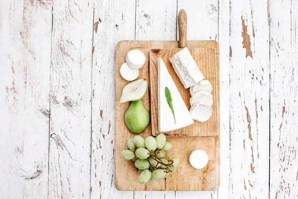 Płyta serowa z serem, gruszką i winogronami na białym w — Zdjęcie stockowe