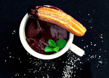 Siyah bir arka plan üzerinde bir fincan ve çikolata sosu ile Churro. 