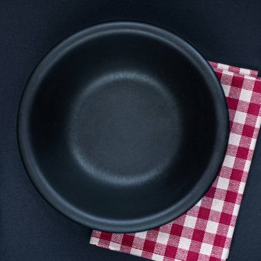 Siyah bir masa üzerinde siyah tabak, çatal bıçak takımı ve kırmızı damalı peçete 