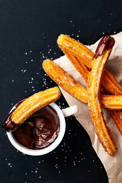 Churros con azúcar sumergido en salsa de chocolate sobre un fondo negro —  Fotos de Stock