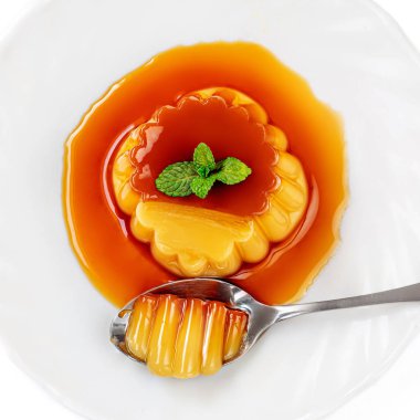 Beyaz pl üzerinde kaşık ve nane ile flan veya karamel muhallebi puding