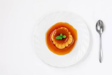 Beyaz pl üzerinde kaşık ve nane ile flan veya karamel muhallebi puding