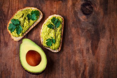Eski ahşap masada yarım yamalak aokado, kopyalama alanı. Avokado sandviçi ve koyu çavdar ekmeği..