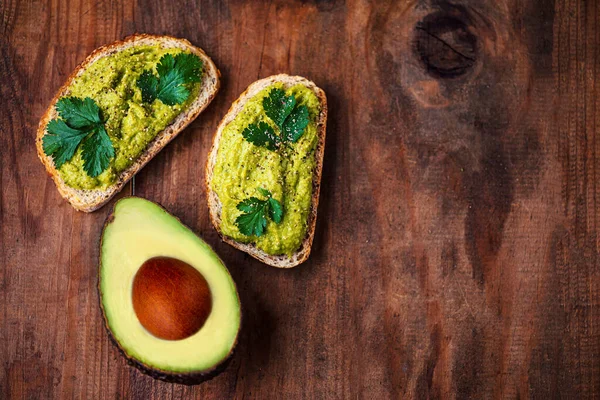 Eski ahşap masada yarım yamalak aokado, kopyalama alanı. Avokado sandviçi ve koyu çavdar ekmeği..