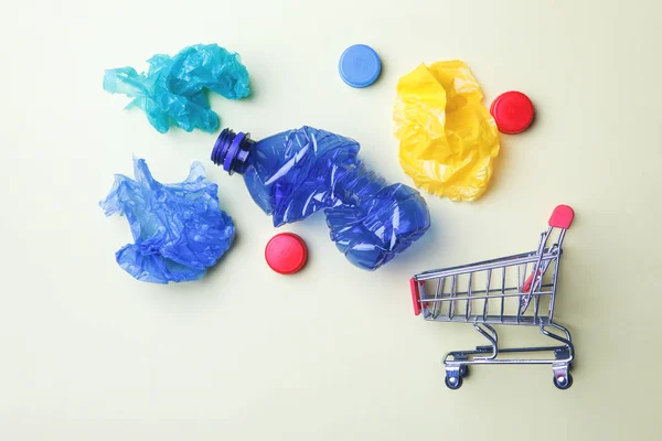 mini shopping trolley full of colorful plastic bags, plastic bottle and caps on yellow background