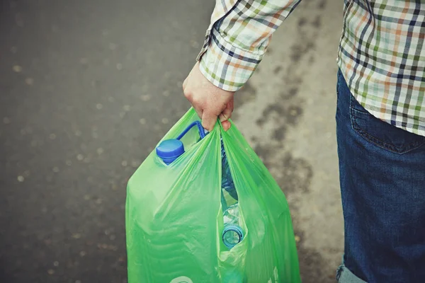 waste management, man\'s hand carrying green plastic bag full of plastic bottles ready for recycling, copy space