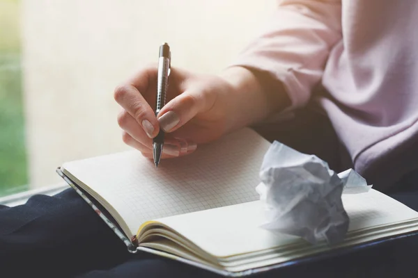 paper ball and woman\'s hands writing something on notebook on her knees