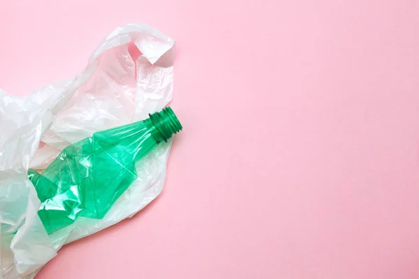 clean crumpled green plastic water bottle and white plastic bag ready for recycling isolated on pink background, top view, minimal background, flat layout, waste management
