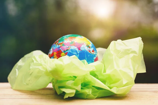 world environment day, earth globe wrapped in transparent plastic bag on wood, copy space