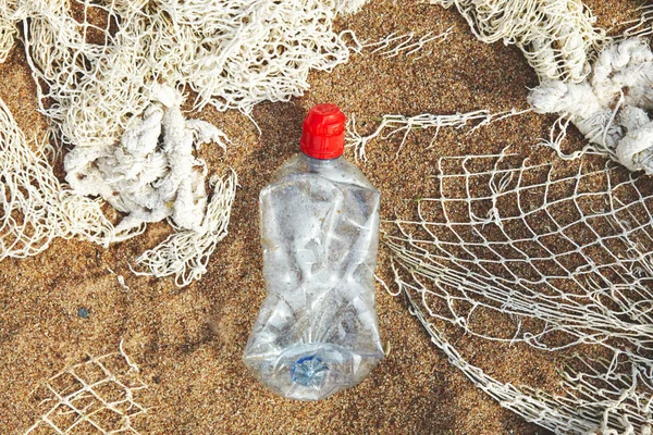environmental problem, plastic pollution concept, dirty used single-use plastic bottle and fishnet on sandy beach